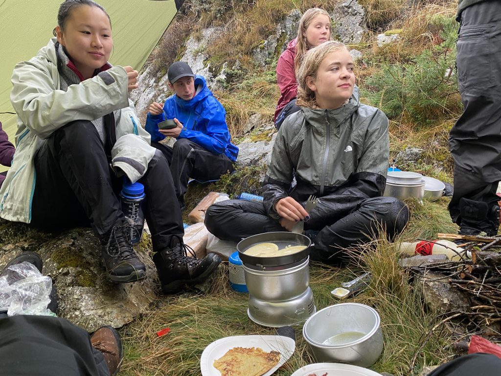 Kristine og Amalie nyter eit måltid ved bålet.
